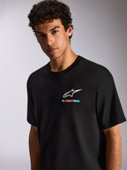 Een man die het Alpinestars Wild Oversized CSF Tee draagt, zwart T-shirt met korte mouwen, voorzien van een wit Astars-logo en levendige meerkleurige branding op de borst, casual motorsport streetwear