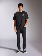 Alpinestars Wild Oversized CSF Tee, T-shirt met korte mouwen, zwart, gedragen door een model met zwarte broek en sneakers, met een wit Astars-logo en levendige meerkleurige branding, casual motorsport streetwear