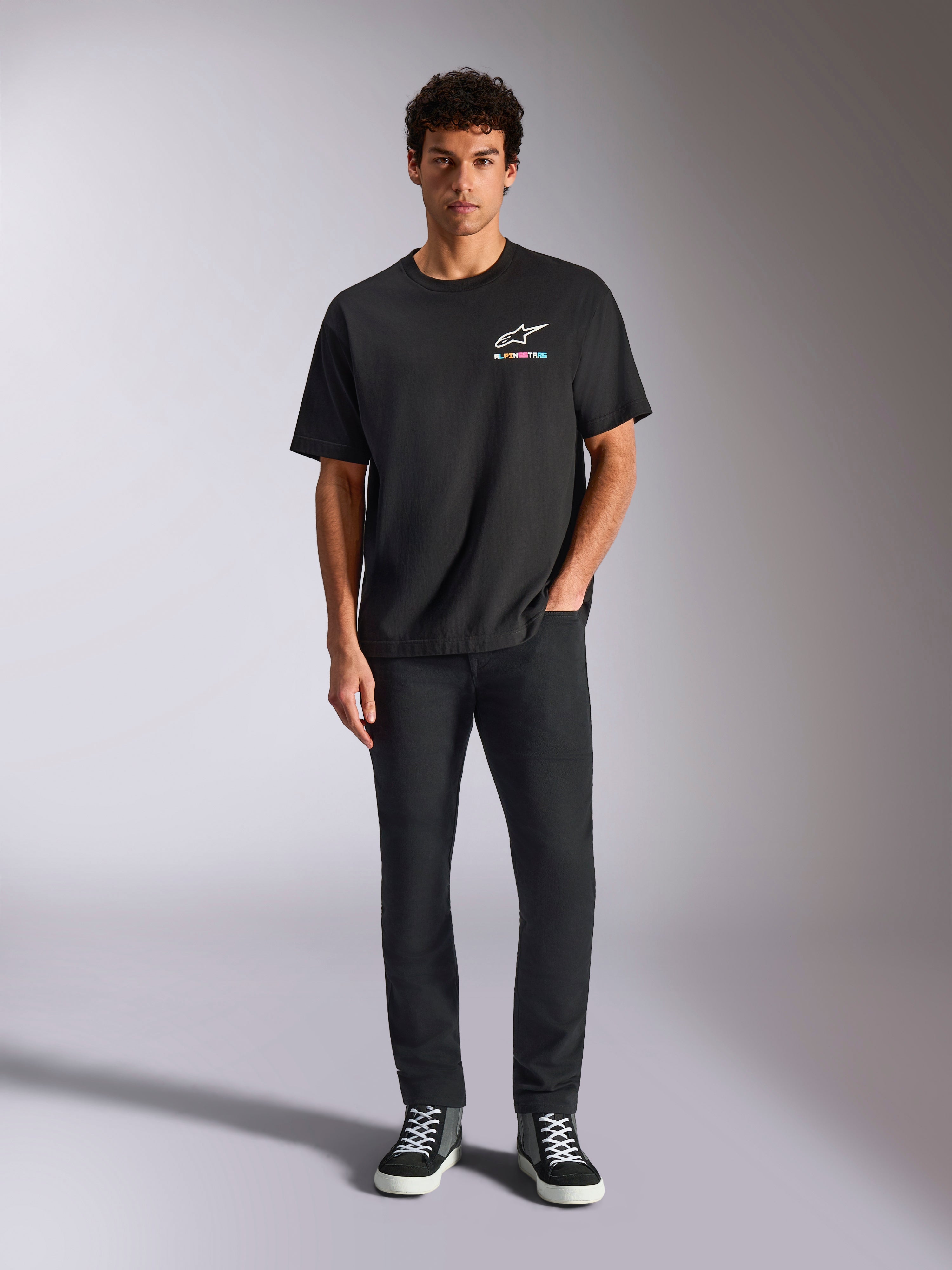 Alpinestars Wild Oversized CSF Tee, T-shirt met korte mouwen, zwart, gedragen door een model met zwarte broek en sneakers, met een wit Astars-logo en levendige meerkleurige branding, casual motorsport streetwear