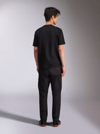 Alpinestars Noka CSF Tee, T-shirt met korte mouwen, zwart, achteraanzicht van model dat het shirt draagt met een zwarte broek en sneakers, casual motorsport streetwear-stijl