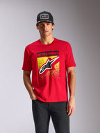 Alpinestars Noka CSF T-shirt, T-shirt met korte mouwen, rood, Astars-logo op de voorkant met geel MX-verloop, gedragen door een mannelijk model met een zwarte Alpinestars pet, casual motorsport streetwear