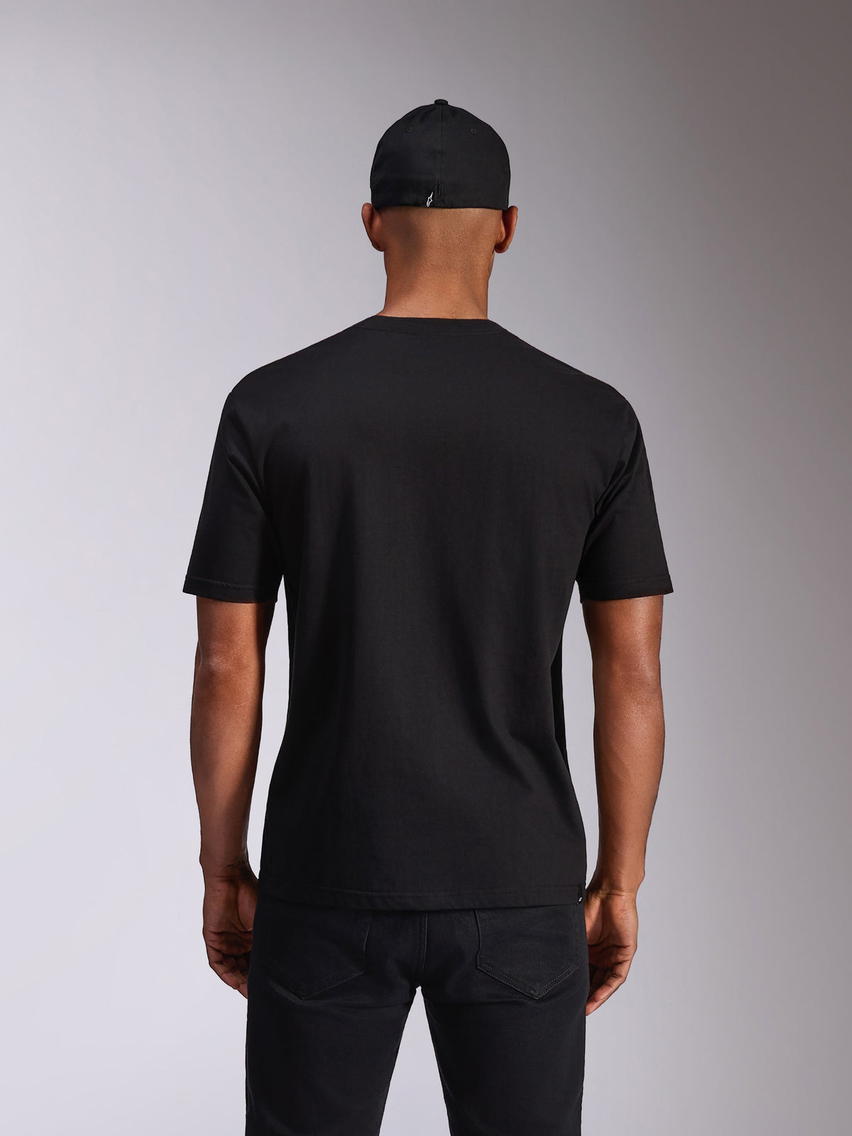 Alpinestars Ellipsoid CSF Tee, t-shirt met korte mouwen, zwart, achteraanzicht op model, gedragen met een zwarte pet en donkere broek, casual motorsport-geïnspireerde streetwear