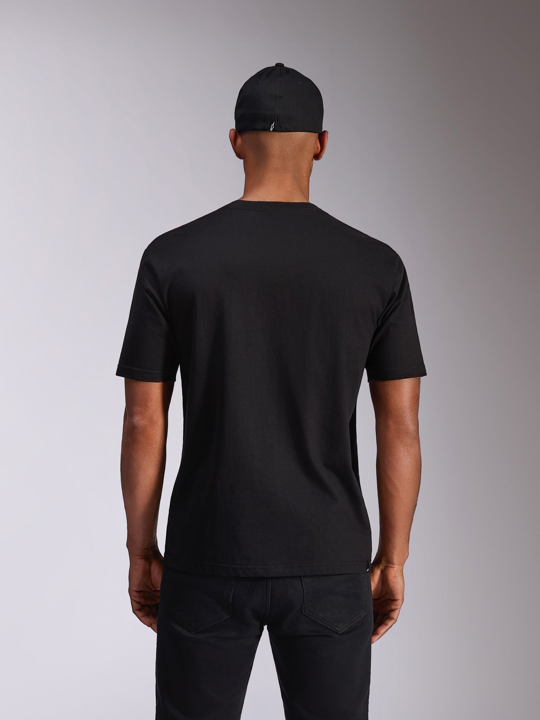 Alpinestars Ellipsoid CSF Tee, kurzärmeliges T-Shirt, Schwarz, Rückansicht am Modell, getragen mit schwarzer Kappe und dunkler Hose, lässige vom Motorsport inspirierte Streetwear