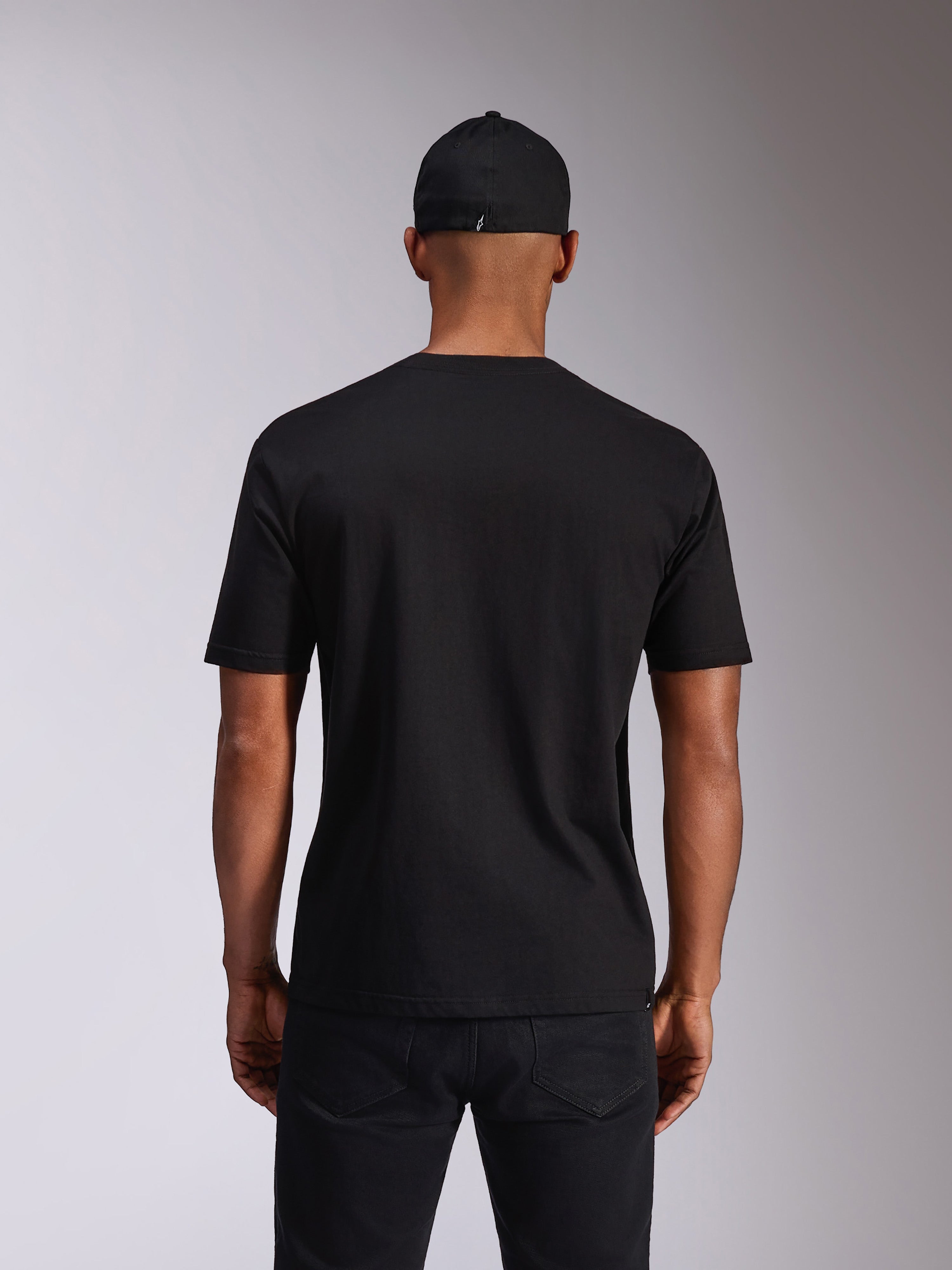 Alpinestars Ellipsoid CSF Tee, t-shirt met korte mouwen, zwart, achteraanzicht op model, gedragen met een zwarte pet en donkere broek, casual motorsport-geïnspireerde streetwear