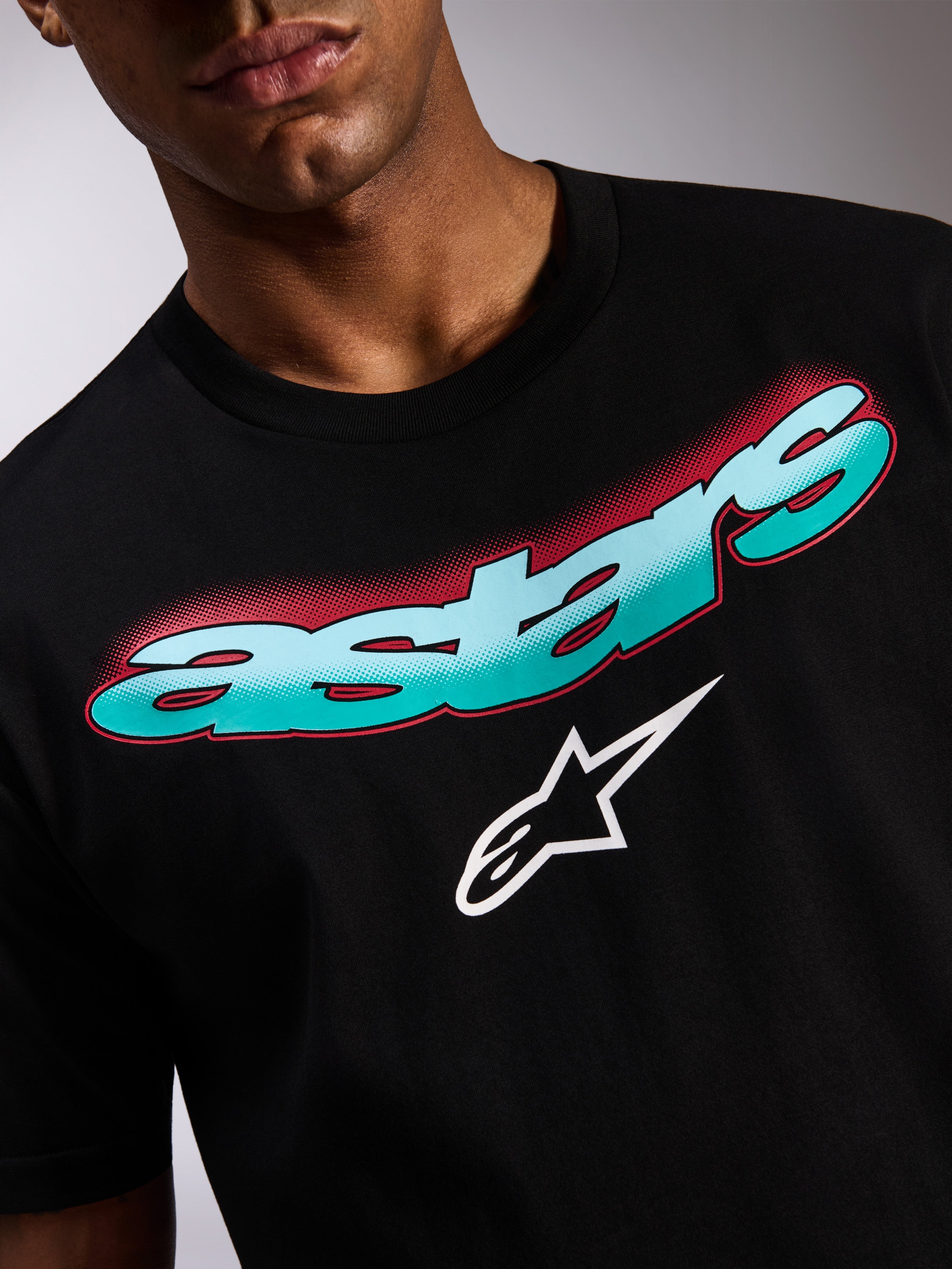 Alpinestars Ellipsoid CSF Tee, T-shirt met korte mouwen, zwart, close-up van de grafische print op de voorzijde met een Astars-woordmerk in een kleurverloop van teal naar blauw, rode halftone-schaduw en wit sterlogo, casual motorsport streetwear