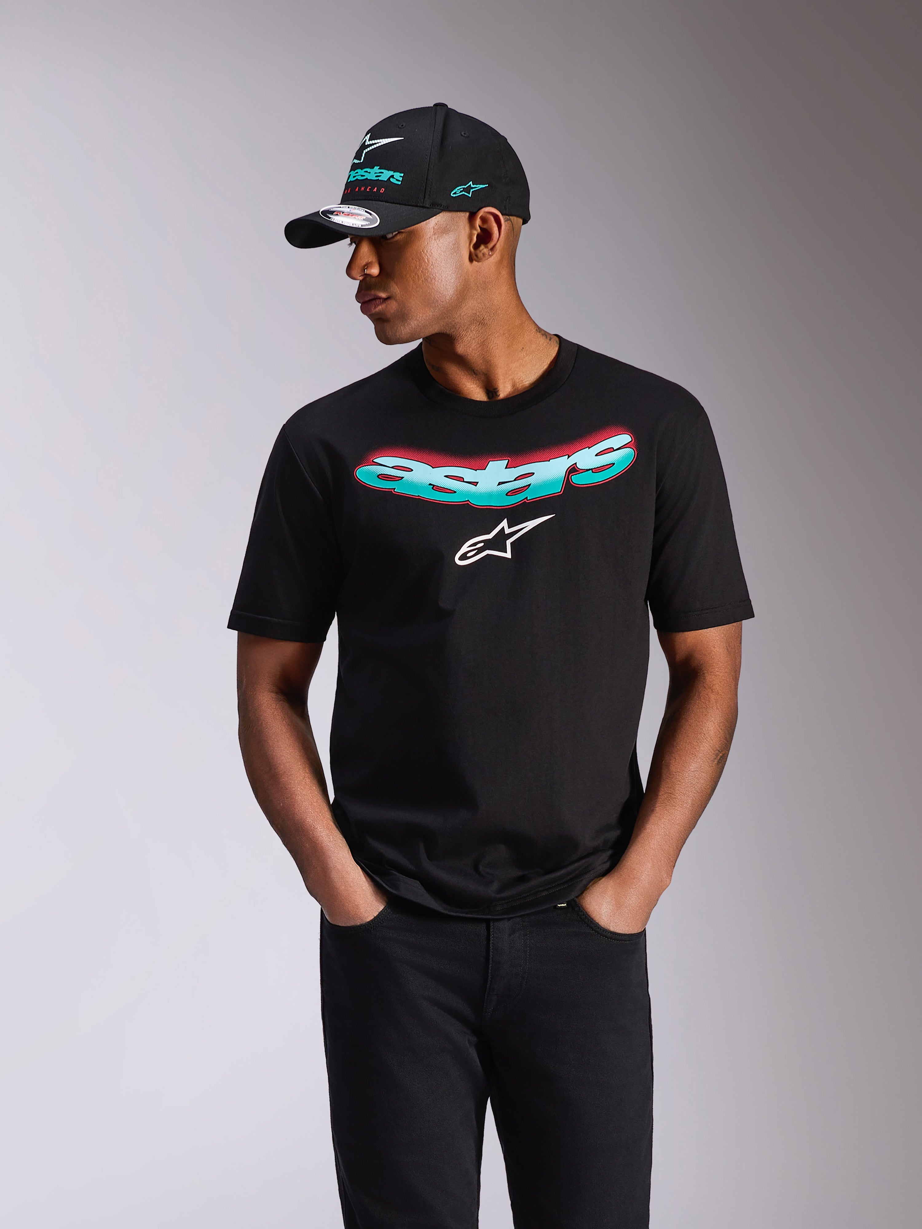 Alpinestars Ellipsoid CSF Tee, T-shirt met korte mouwen, zwart, Astars-woordmerk met teal en roze kleurverloop en wit logo, gedragen door een model met bijpassende Alpinestars-pet en zwarte jeans, casual motorsport streetwear