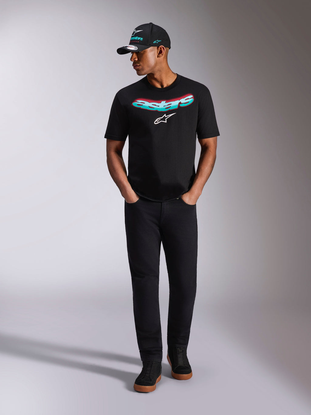 Alpinestars Ellipsoid CSF Tee, T-shirt met korte mouwen, zwart, gebogen Astars-woordmerk met een kleurverloop van teal en roze en een wit logo, gedragen door een model met bijpassende zwarte pet en broek, casual motorsport lifestyle kleding