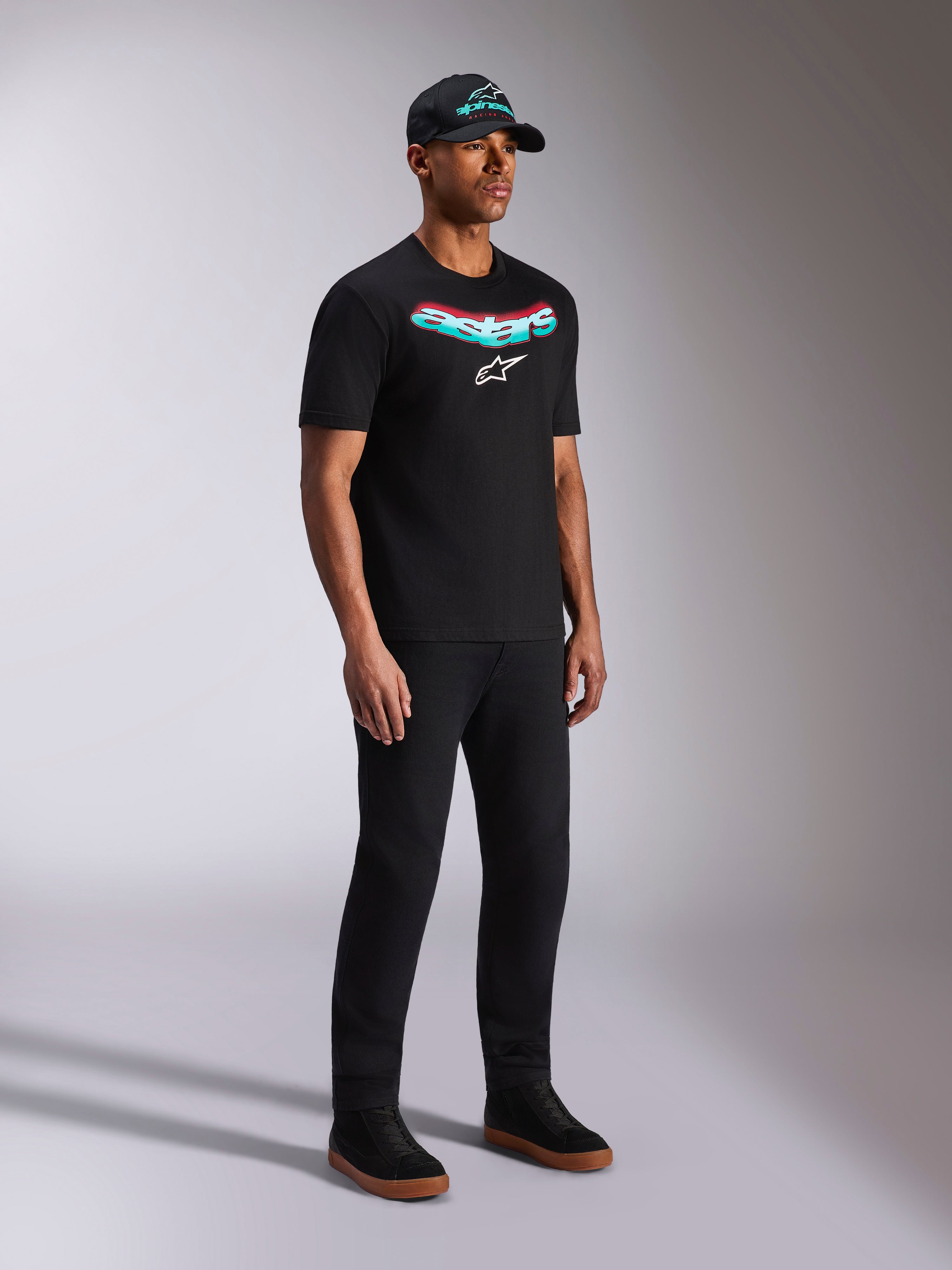 Alpinestars Ellipsoid CSF Tee, zwart T-shirt met korte mouwen, Astars-graphic met groenblauw en rood kleurverloop en wit logo, mannelijk model in casual streetwear met zwarte pet en broek