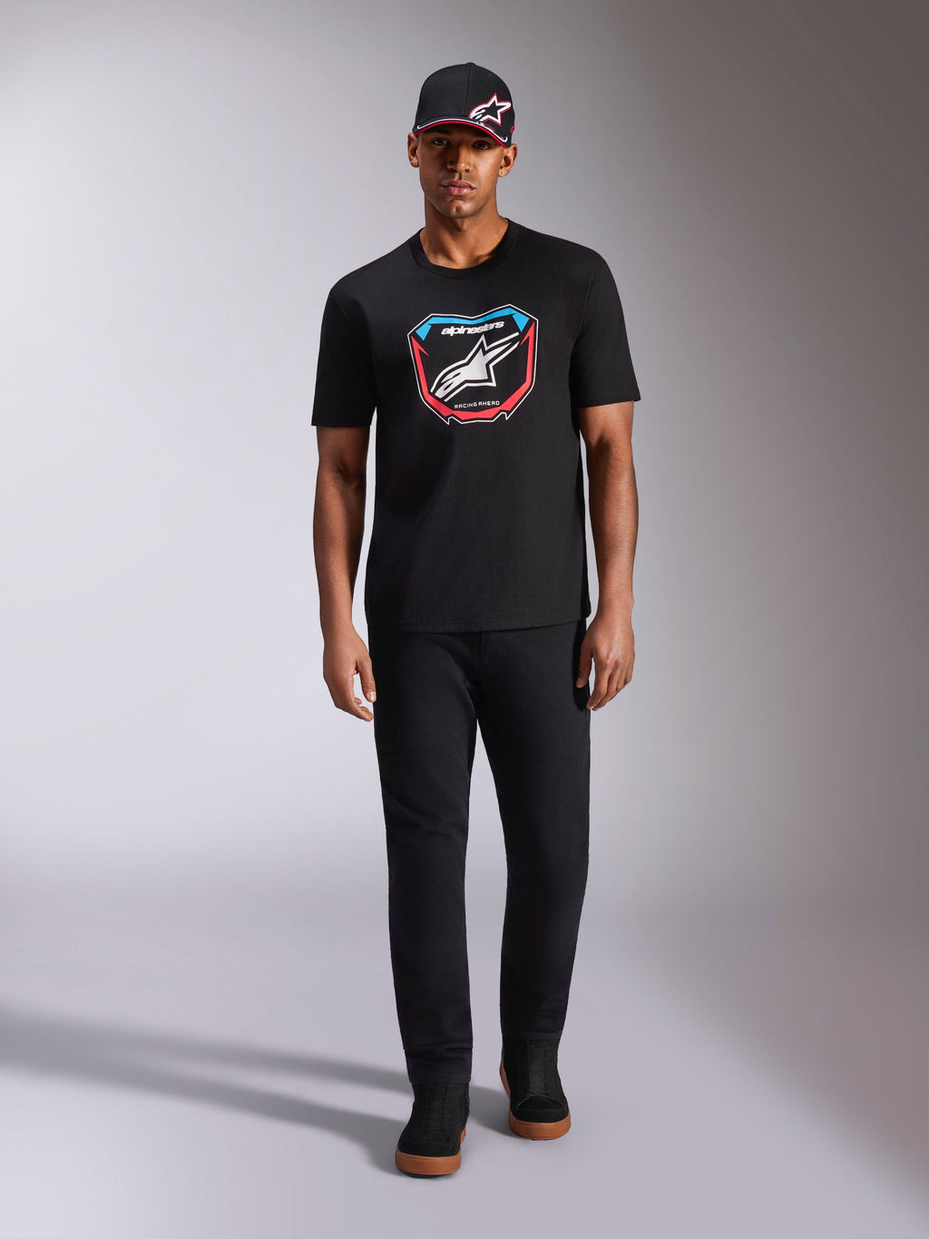 Alpinestars Plate CSF Tee, T-shirt met korte mouwen, zwart, MX-plaat graphic aan de voorkant met wit Astars-logo en blauwe en rode accenten, gedragen door model met bijpassende zwarte pet en broek, casual motorsport sportkleding