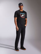 Alpinestars Plate CSF Tee, T-shirt met korte mouwen, zwart, kleurrijke MX-plaat graphic met sterlogo aan de voorzijde, gedragen door model met zwarte logopet en broek, casual motorsport-geïnspireerde streetwear