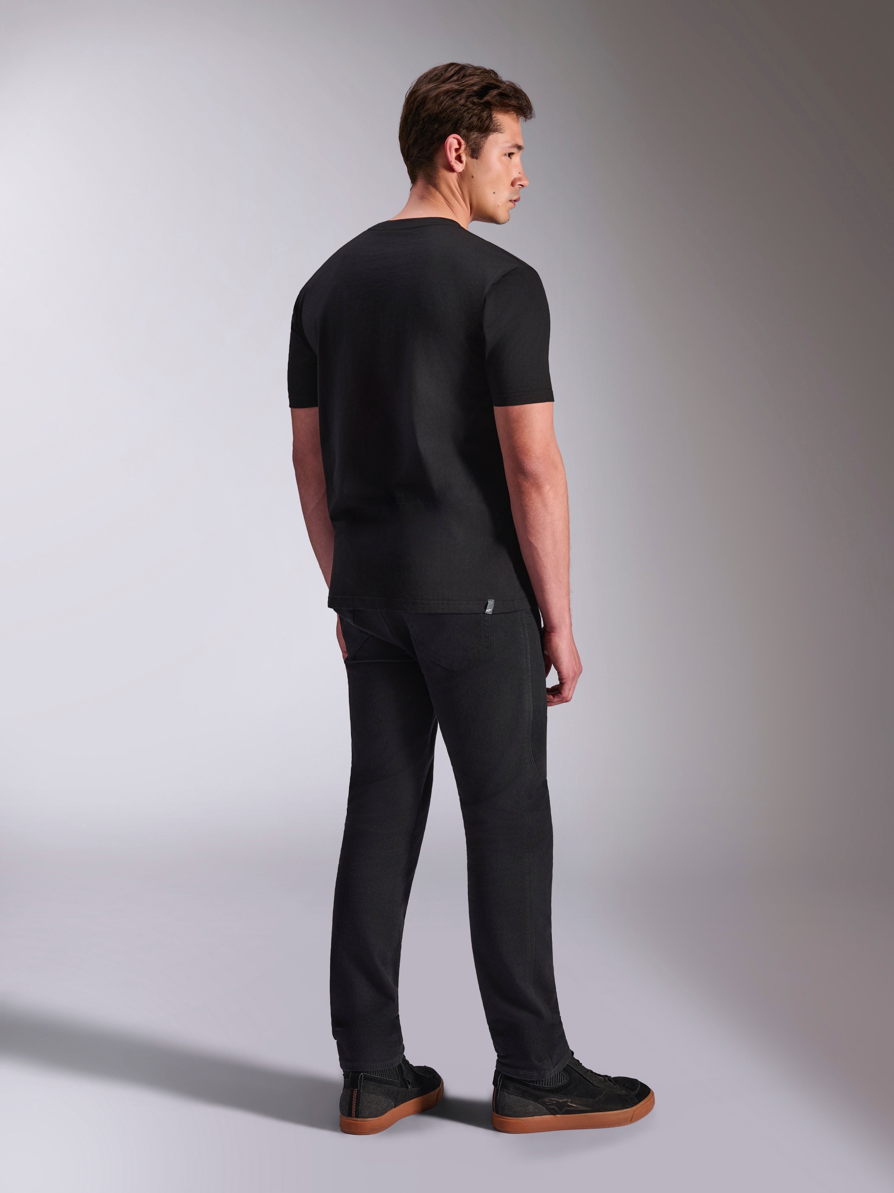 Alpinestars Abus CSF Tee, T-shirt met korte mouwen, zwart, achteraanzicht op mannelijk model, casual motorsport streetwear, gecombineerd met een donkere broek en sneakers