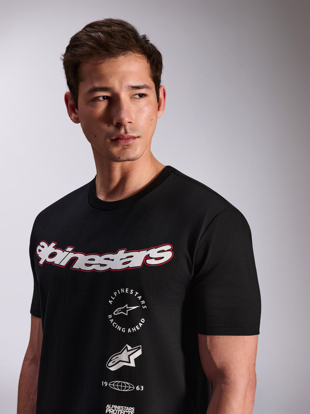 Alpinestars Abus CSF Tee, T-shirt met korte mouwen, zwart, gedragen door een model, voorzien van een wit Alpinestars script-logo met rode omtrek en gestapelde grafische logo's op de borst, casual motorsport streetwear