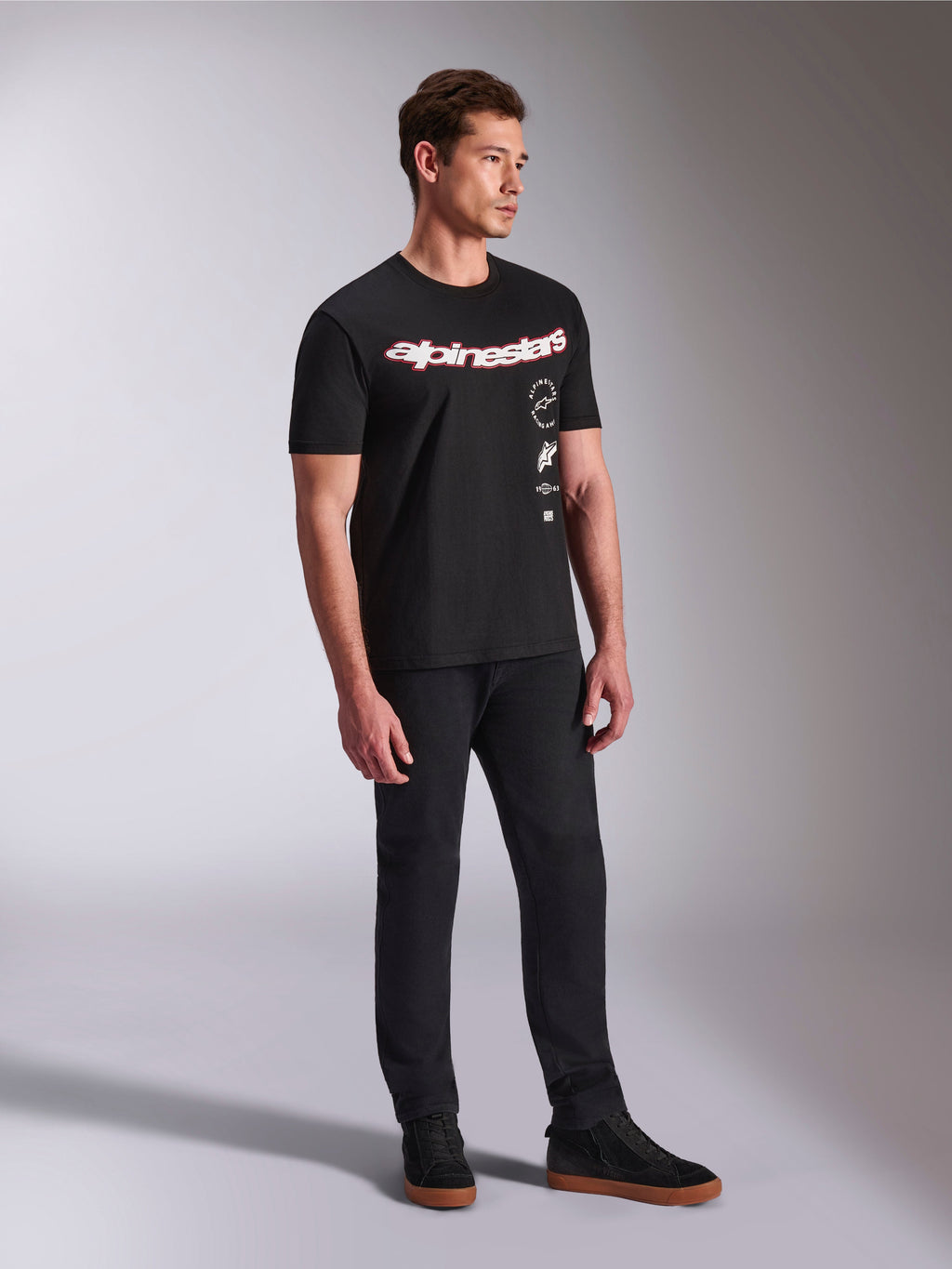 Alpinestars Abus CSF Tee, T-shirt met korte mouwen, zwart, met gebogen rood en wit Alpinestars-logo en verticaal gestapelde graphics, gedragen met zwarte broek en sneakers, casual streetwear geïnspireerd op motorsport
