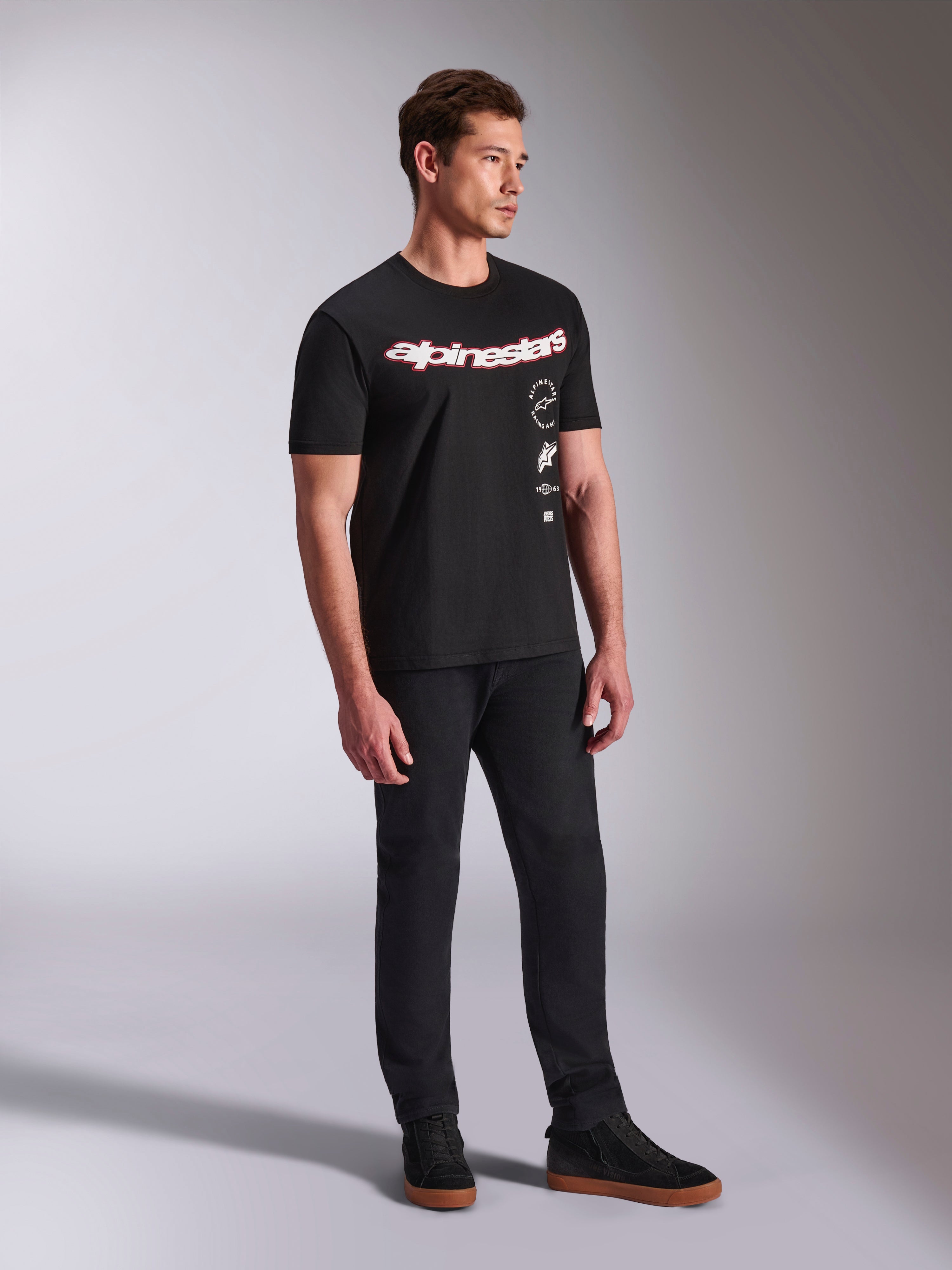 Alpinestars Abus CSF Tee, T-shirt met korte mouwen, zwart, met gebogen rood en wit Alpinestars-logo en verticaal gestapelde graphics, gedragen met zwarte broek en sneakers, casual streetwear geïnspireerd op motorsport