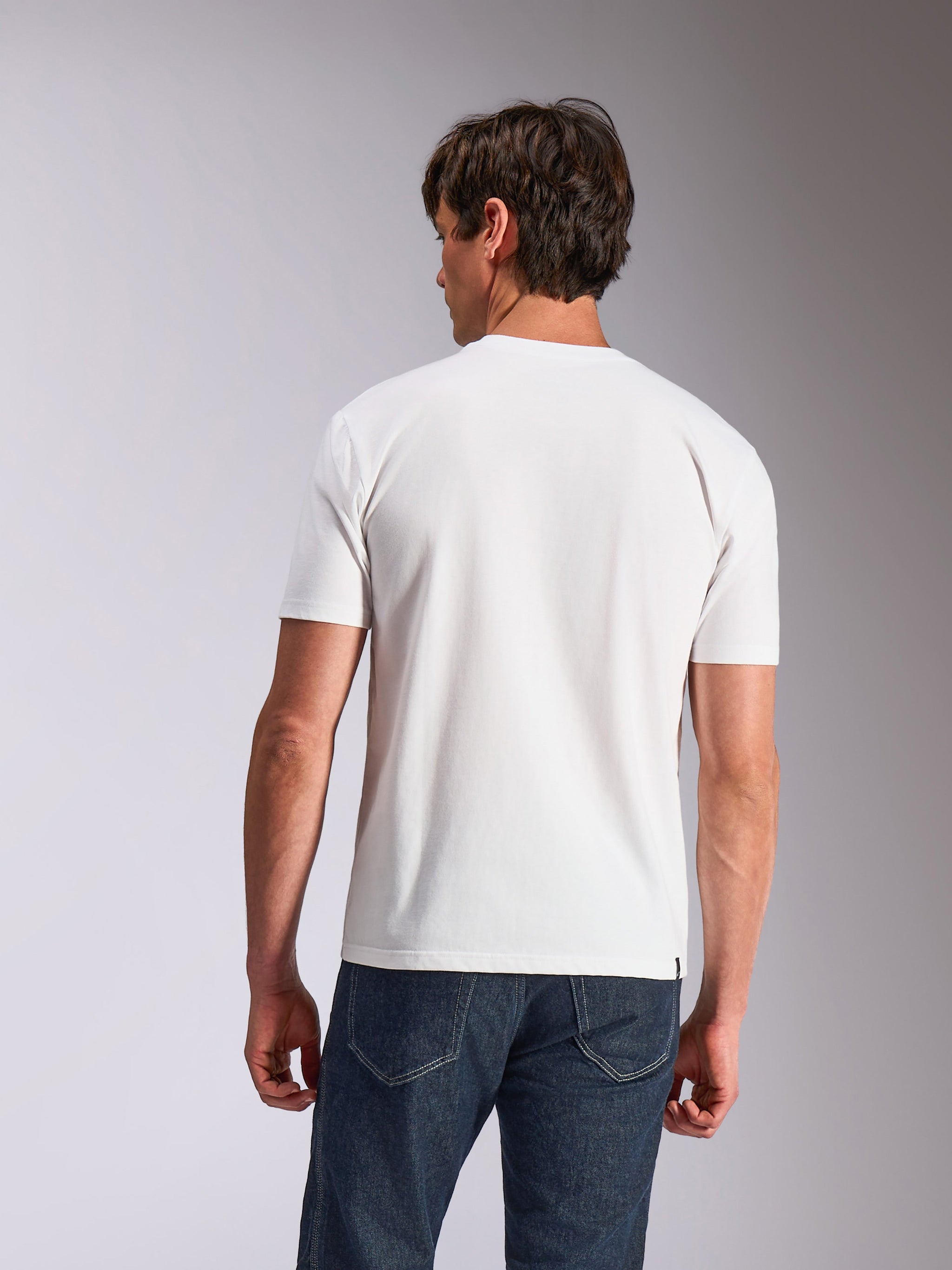 Alpinestars Abus CSF Tee, t-shirt à manches courtes, blanc, vue de dos d'un mannequin portant un t-shirt blanc uni et un jean bleu foncé, vêtement lifestyle décontracté inspiré par les sports mécaniques