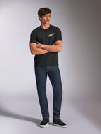 Alpinestars Angler CSF Tee, T-shirt met korte mouwen, zwart, levendig meerkleurig Astars-logo op de borst, gedragen door een model met de armen over elkaar, donkere denim jeans en zwarte sneakers, casual motorsport streetwear