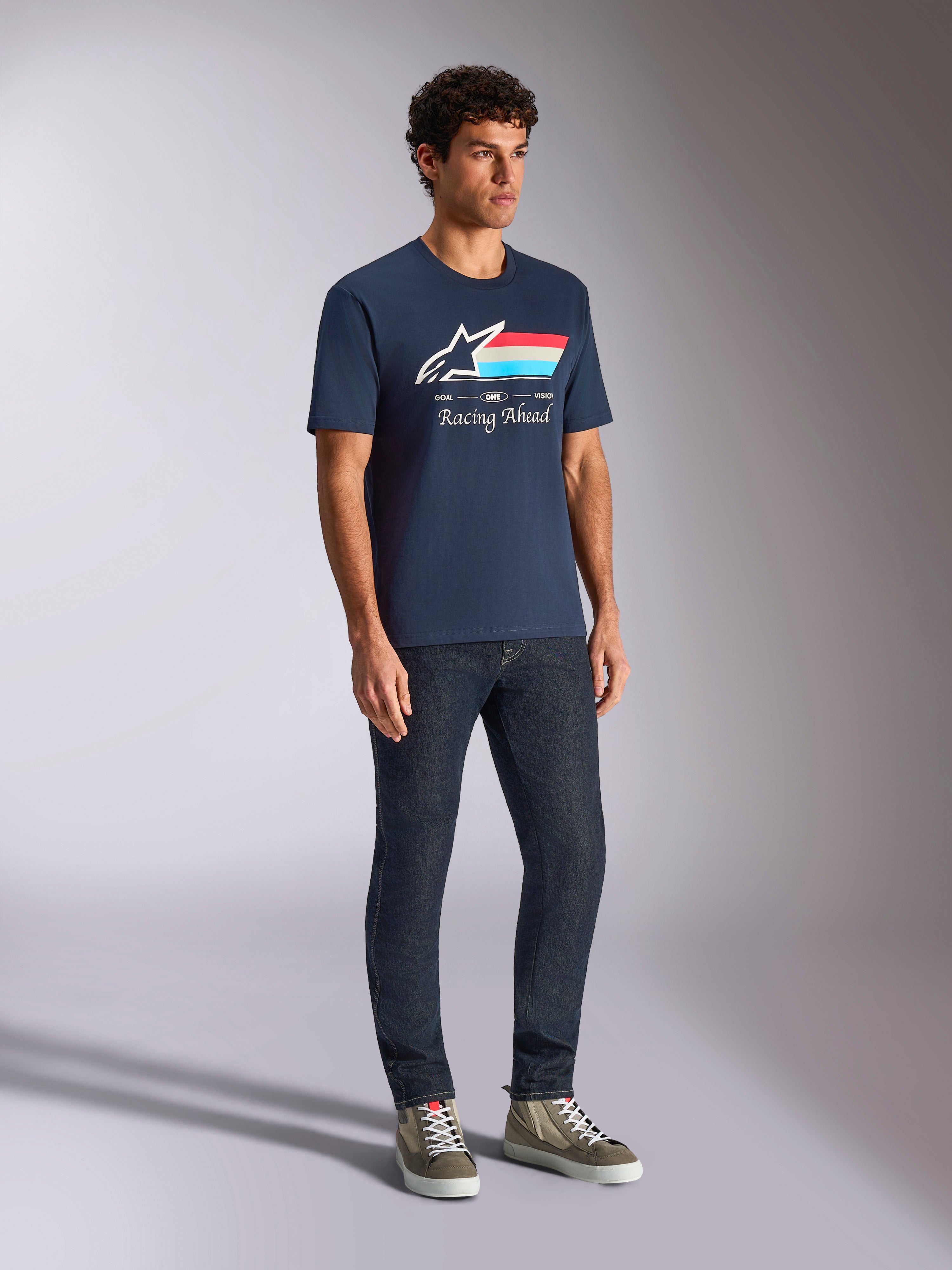 Alpinestars Trifecta CSF Tee, T-shirt met korte mouwen, marineblauw, voorzien van Astars-logo met driekleurige strepen en 'Racing Ahead'-tekst, gedragen door een model met donkere jeans en sneakers, casual door motorsport geïnspireerde streetwear