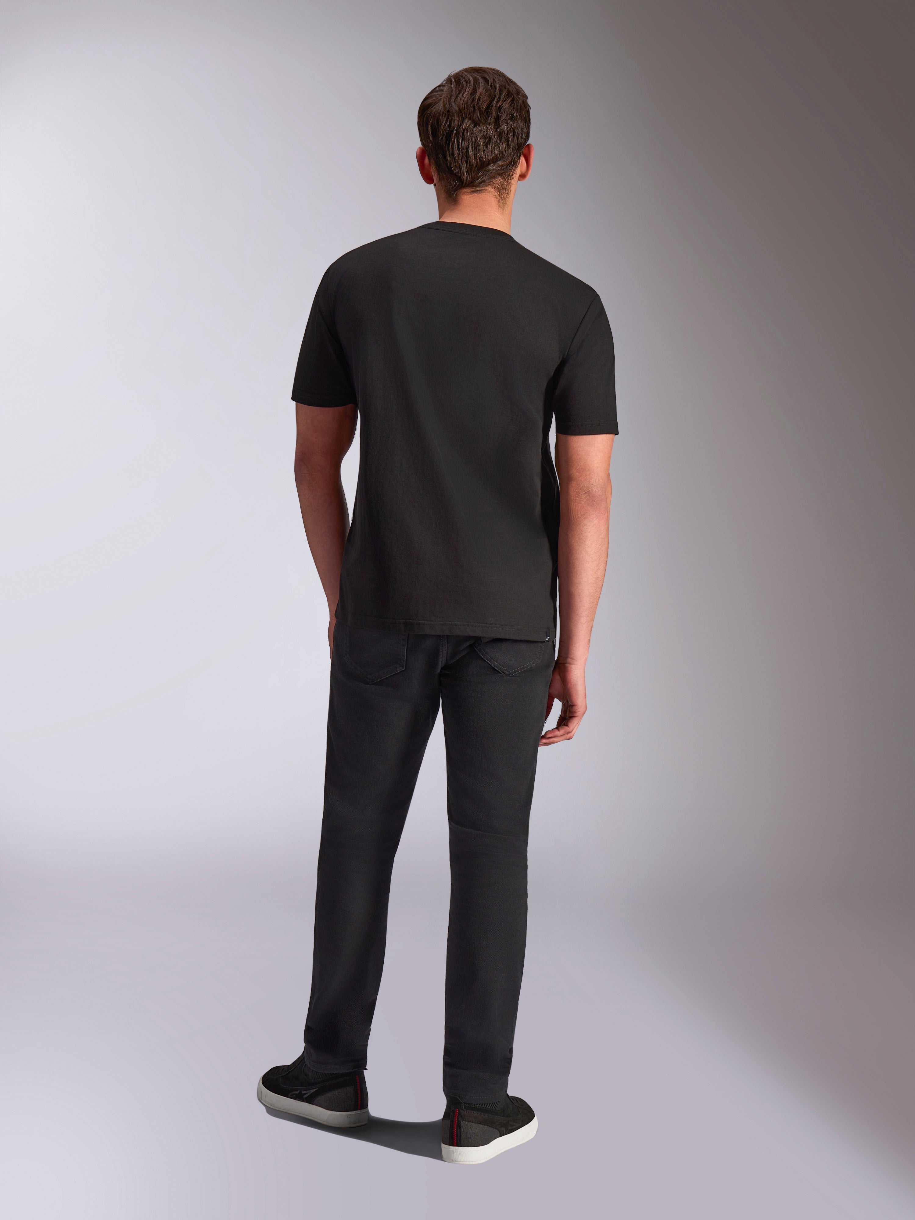 Alpinestars Trifecta CSF Tee, T-shirt met korte mouwen, zwart, achteraanzicht op mannelijk model, gedragen met zwarte broek en zwarte sneakers, casual op de motorsport geïnspireerde streetwear