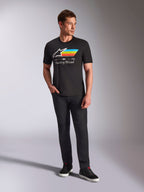 Alpinestars Trifecta CSF Tee, T-shirt met korte mouwen, zwart, met een wit Astars-logo met cyaan, gele en oranje strepen en 'Racing Ahead'-tekst, gedragen door een model met een zwarte broek en sneakers voor casual motorsport streetwear