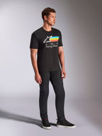 Alpinestars Trifecta CSF Tee, T-shirt met korte mouwen, zwart, wit Astars-logo met blauwe, gele en oranje strepen en 'Racing Ahead'-graphic, gedragen door een model met een zwarte broek en sneakers, casual motorsport-geïnspireerde lifestyle-kleding