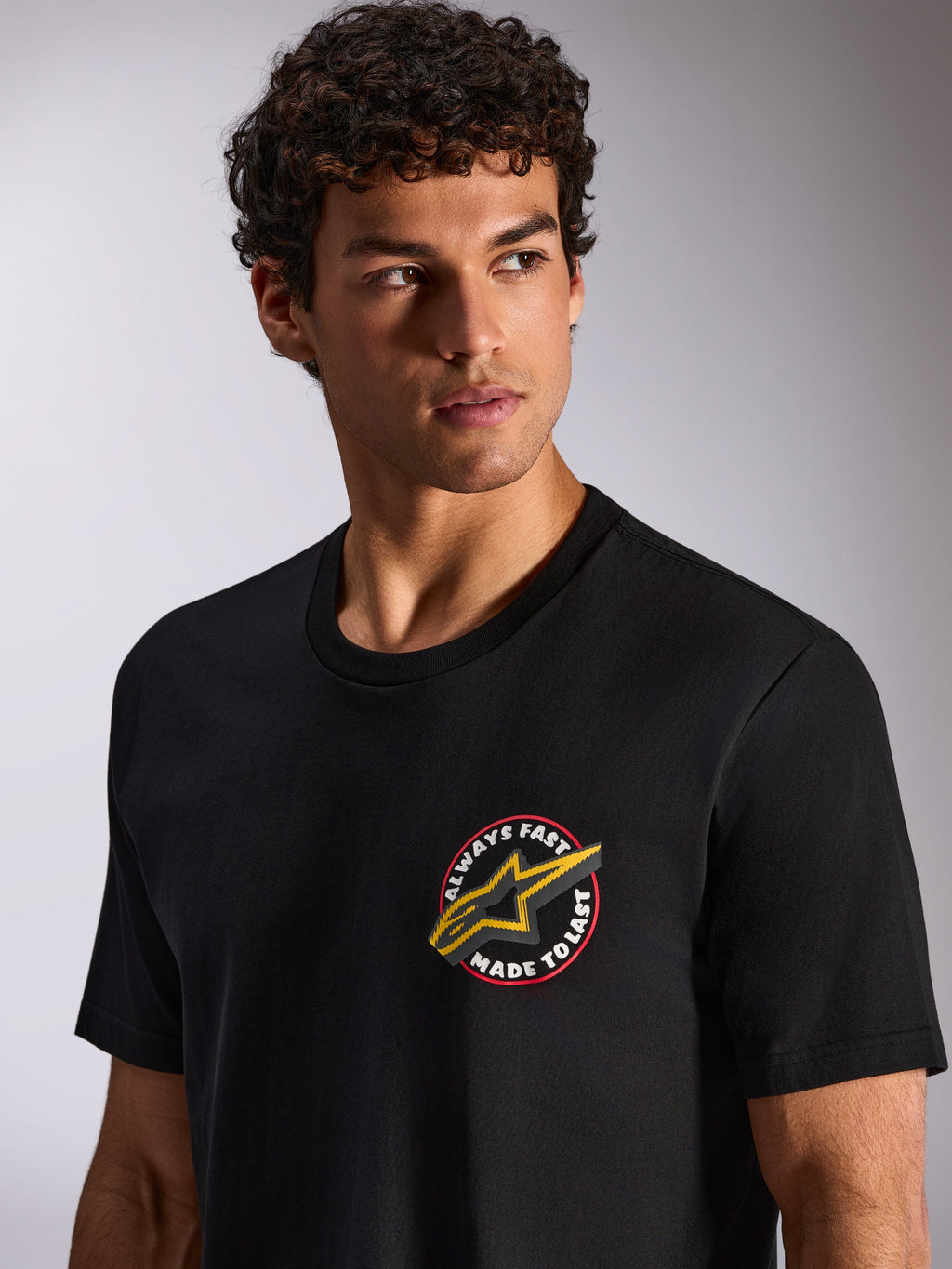 Alpinestars Aorbit CSF Tee, t-shirt met korte mouwen, zwart, ronde grafische opdruk op de borst met "Always Fast Made to Last" en geel Astars-logo, gedragen door model, casual motorsport streetwear