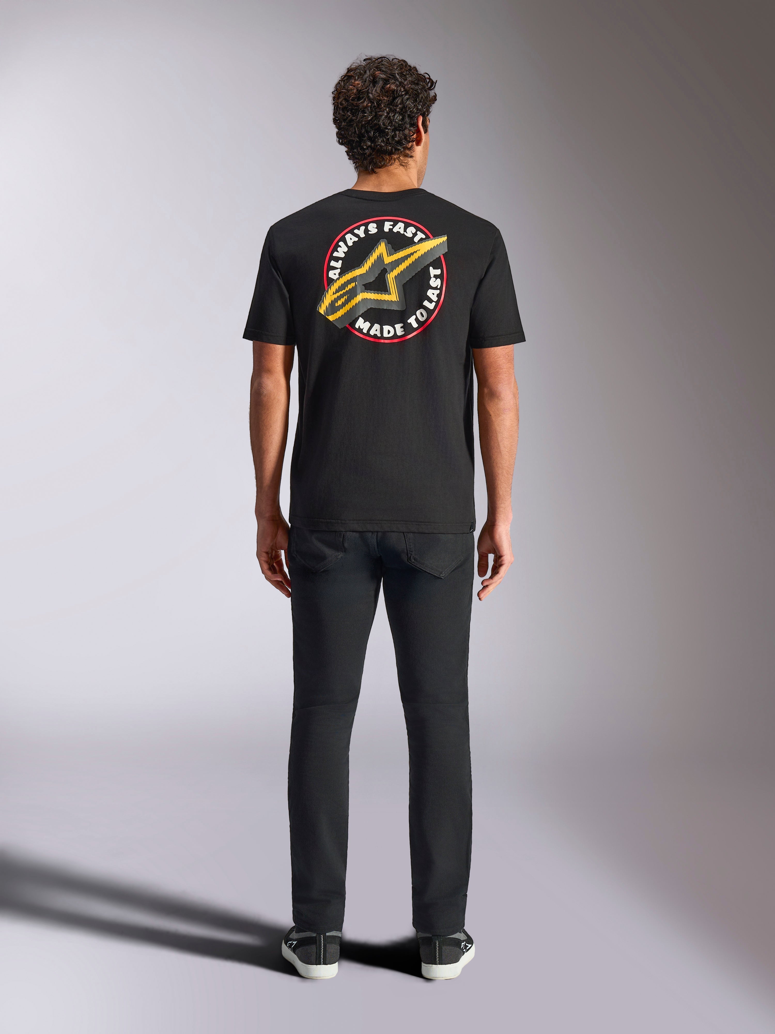 Alpinestars Aorbit CSF Tee, T-shirt met korte mouwen, zwart, van achteren gezien op een model met een zwarte broek, voorzien van een grote 'Always Fast Made to Last' opdruk met geel Astars-logo, casual motorsport streetwear