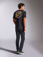 Alpinestars Aorbit CSF Tee, T-shirt met korte mouwen, zwart, achteraanzicht met een groot geel Astars-logo en ronde 'Always Fast Made to Last' grafische print, gedragen met zwarte jeans en casual sneakers, motorsport-geïnspireerde streetwear-stijl