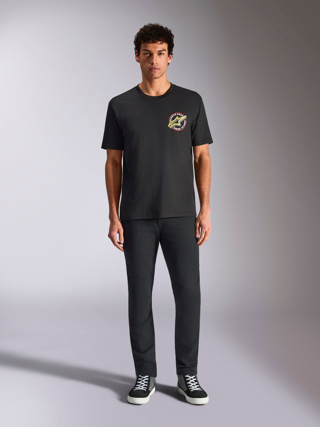 Alpinestars Aorbit CSF Tee, T-shirt met korte mouwen, zwart, circulair logo met 'Always Fast Made to Last'-tekst op de borst, gedragen door een model met zwarte broek en sneakers, casual motorsport-geïnspireerde streetwear