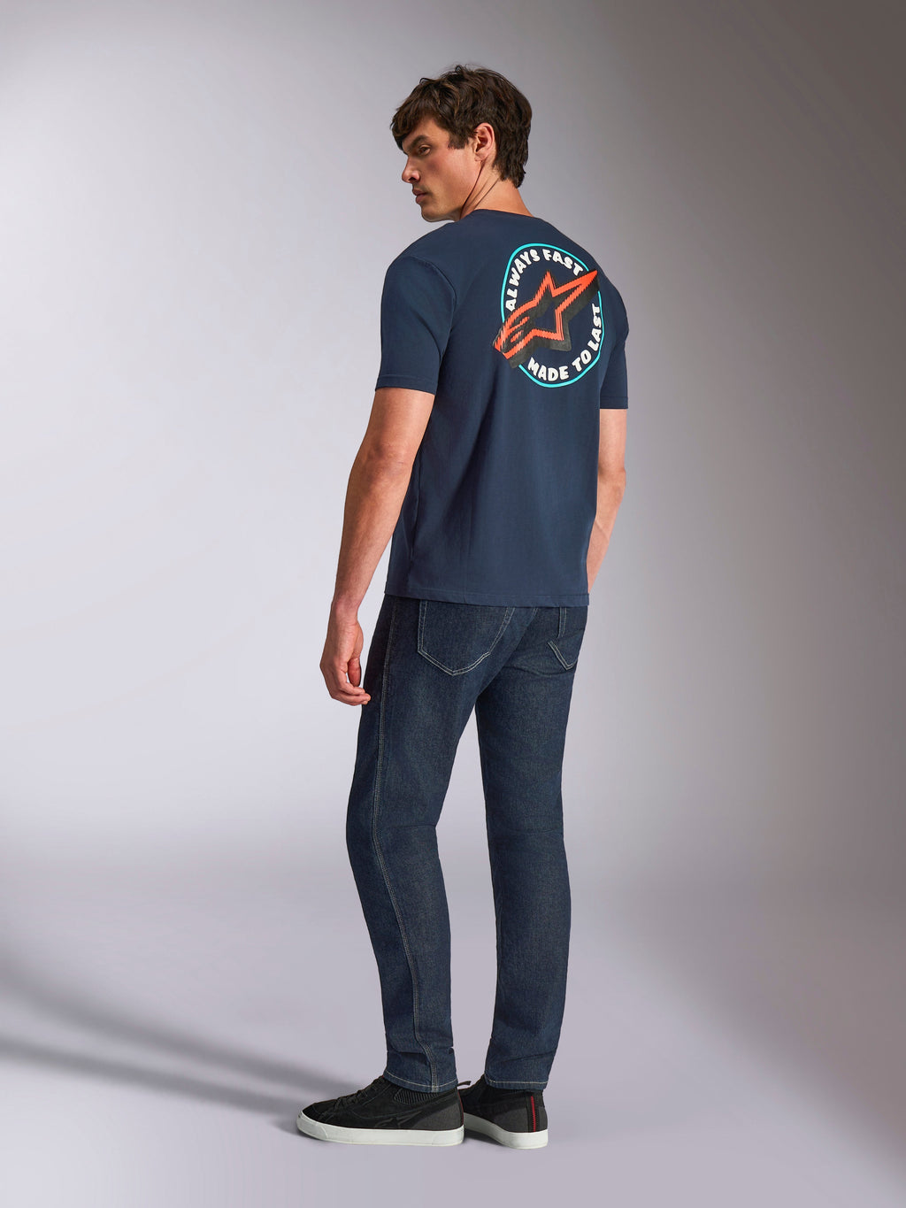 Alpinestars Aorbit CSF Tee, T-shirt met korte mouwen, marineblauw, achteraanzicht op model met groot cirkelvormig Astars-logo en 'Always Fast Made to Last' graphic, casual motorsport-geïnspireerde streetwear