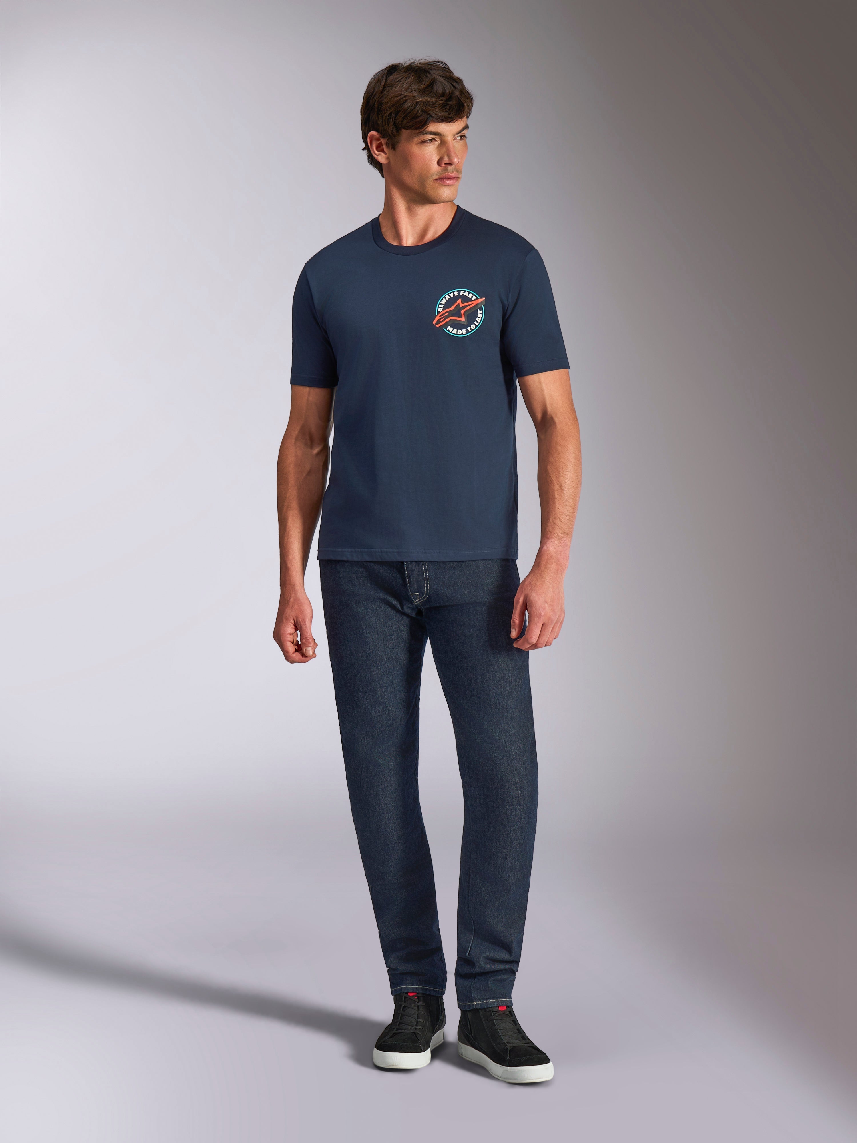 Alpinestars Aorbit CSF Tee, T-shirt met korte mouwen, donkerblauw, ronde borstgraphic met 'Always Fast Made to Last'-tekst, gedragen met donkere jeans en sneakers, casual motorsport lifestyle-kleding