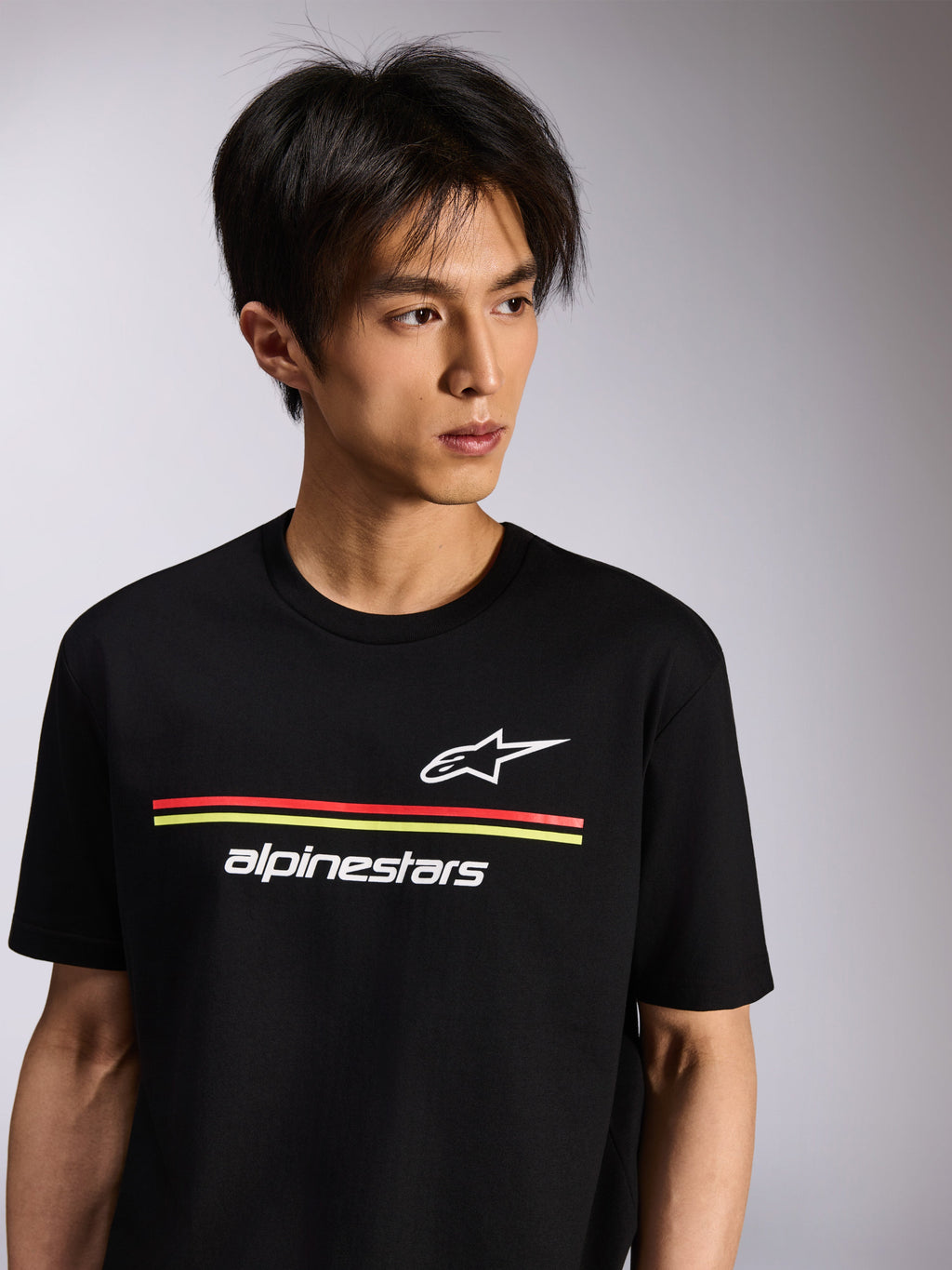 Alpinestars Lanes CSF Tee, T-shirt met korte mouwen, zwart, met witte Astars- en Alpinestars-logo's met rode en gele strepen, casual motorsport streetwear gedragen door een model