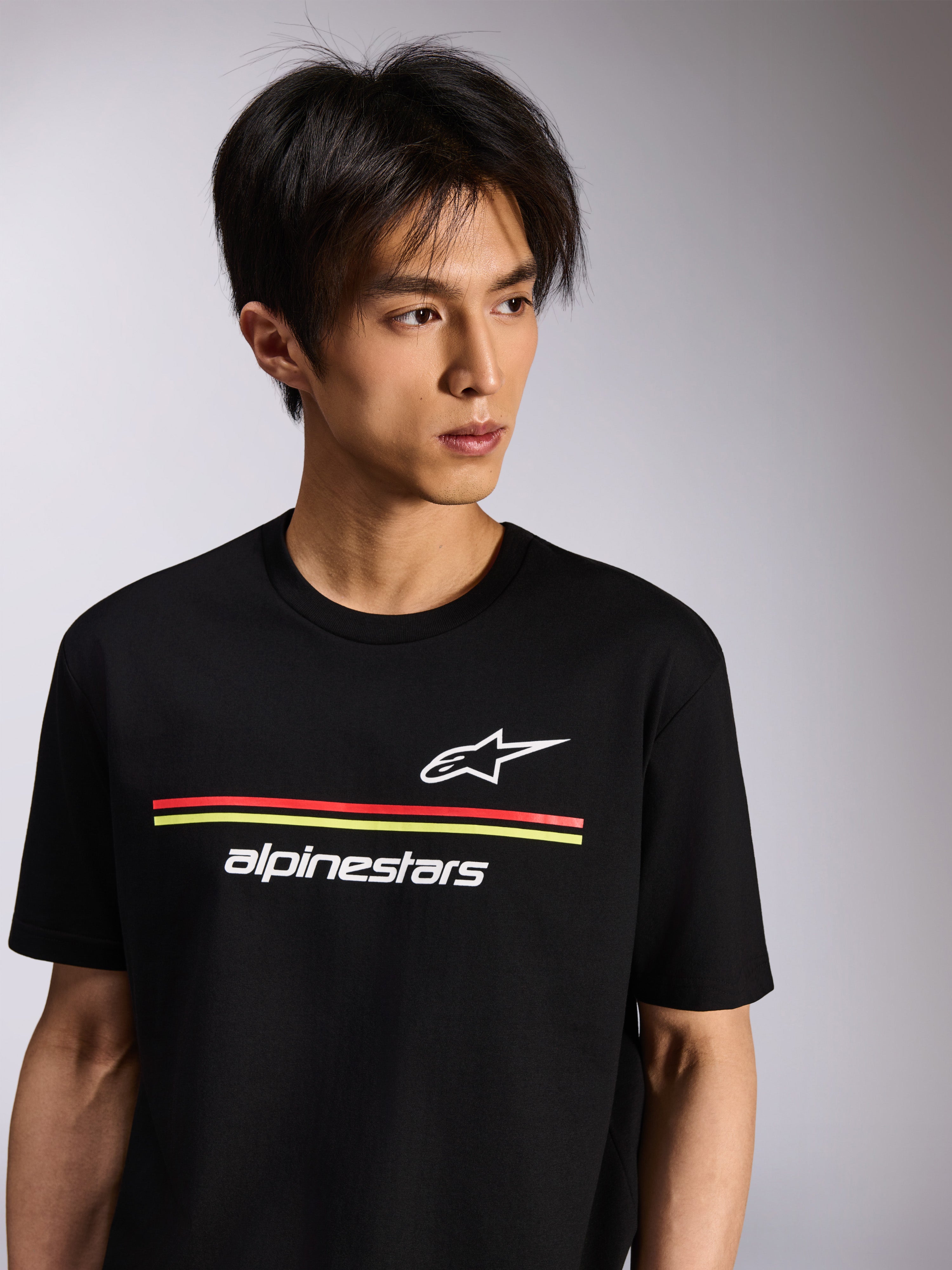 Alpinestars Lanes CSF Tee, T-shirt met korte mouwen, zwart, met witte Astars- en Alpinestars-logo's met rode en gele strepen, casual motorsport streetwear gedragen door een model