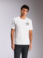 Alpinestars Order CSF Tee, T-shirt met korte mouwen, wit, borstprint met helm en palmbomen, gedragen door model met donkere broek, casual motorsport-geïnspireerde streetwear
