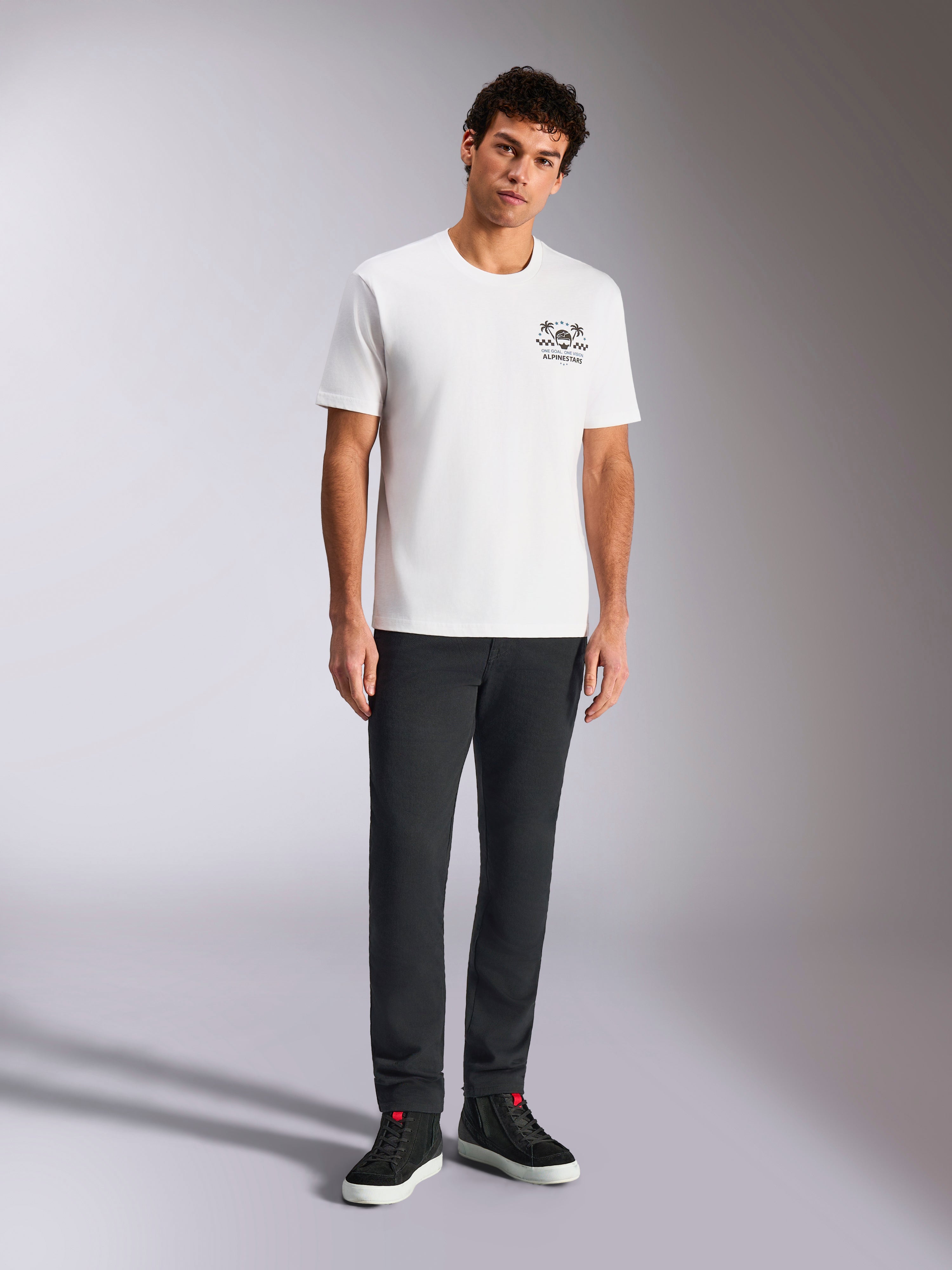 Alpinestars Order CSF Tee, T-shirt met korte mouwen, wit, kleine zwarte graphic op de borst met helm en palmbomen, casual motorsport streetwear, gedragen door model met zwarte broek en sneakers