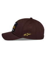 Alpinestars Matrix Snapback pet, bruin, zijaanzicht, gebogen klep met zwart koorddetail, geborduurde patch aan de voorzijde, geel Astars-logo aan de zijkant, gestructureerde katoenen twill-constructie, casual motorsport pet