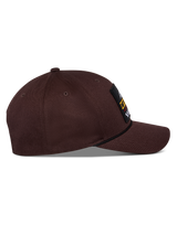 Alpinestars Matrix Snapback pet, donkerbruin, zijaanzicht met gebogen klep, gestructureerde kroon en logopatch aan de voorzijde met touwdetail, casual motorsport-geïnspireerde hoofdbedekking