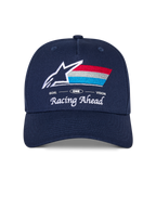 Alpinestars Trifecta Snapback pet, marineblauwe cap met gebogen klep, voorzien van geborduurd logo voorop met witte ster en driekleurige strepen, 'Racing Ahead' en 'Goal One Vision' witte tekst, gestructureerde kroon, casual motorsport-geïnspireerde pet