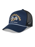 Alpinestars Finisher Trucker pet, marineblauw en zwart, gebogen klep met wit koorddetail, Alpinestars grafische print met geblokte vlaggen, gouden logo en 'Racing Ahead' tekst op de voorkant, Astars logo-borduurwerk aan de zijkant, casual motorsport-hoofdbedekking