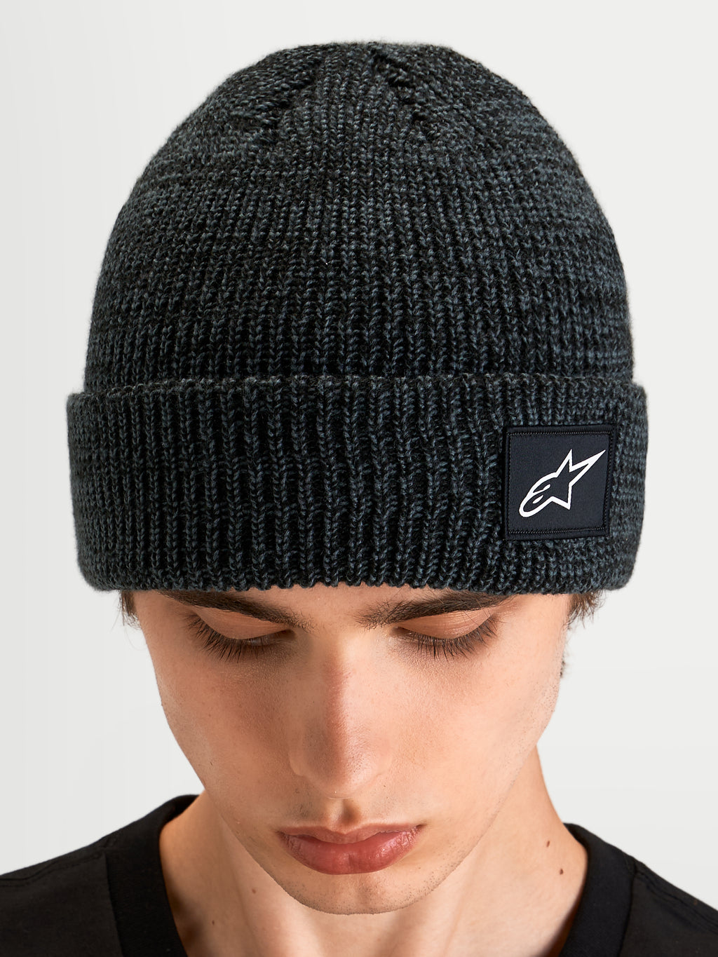 Alpinestars Bonnet Unload Rib Cuff, bonnet sportswear en maille côtelée gris anthracite chiné avec écusson du logo Alpinestars, porté en gros plan sur un modèle