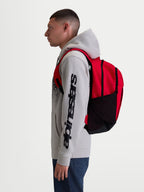 Alpinestars GFX Boss rugzak, rode en zwarte sportswear dagrugzak van 20L, duurzaam 600D polyester met zijvakken van mesh en gevoerde luchtmesh schouderbanden, getoond op een model voor dagelijks gebruik.