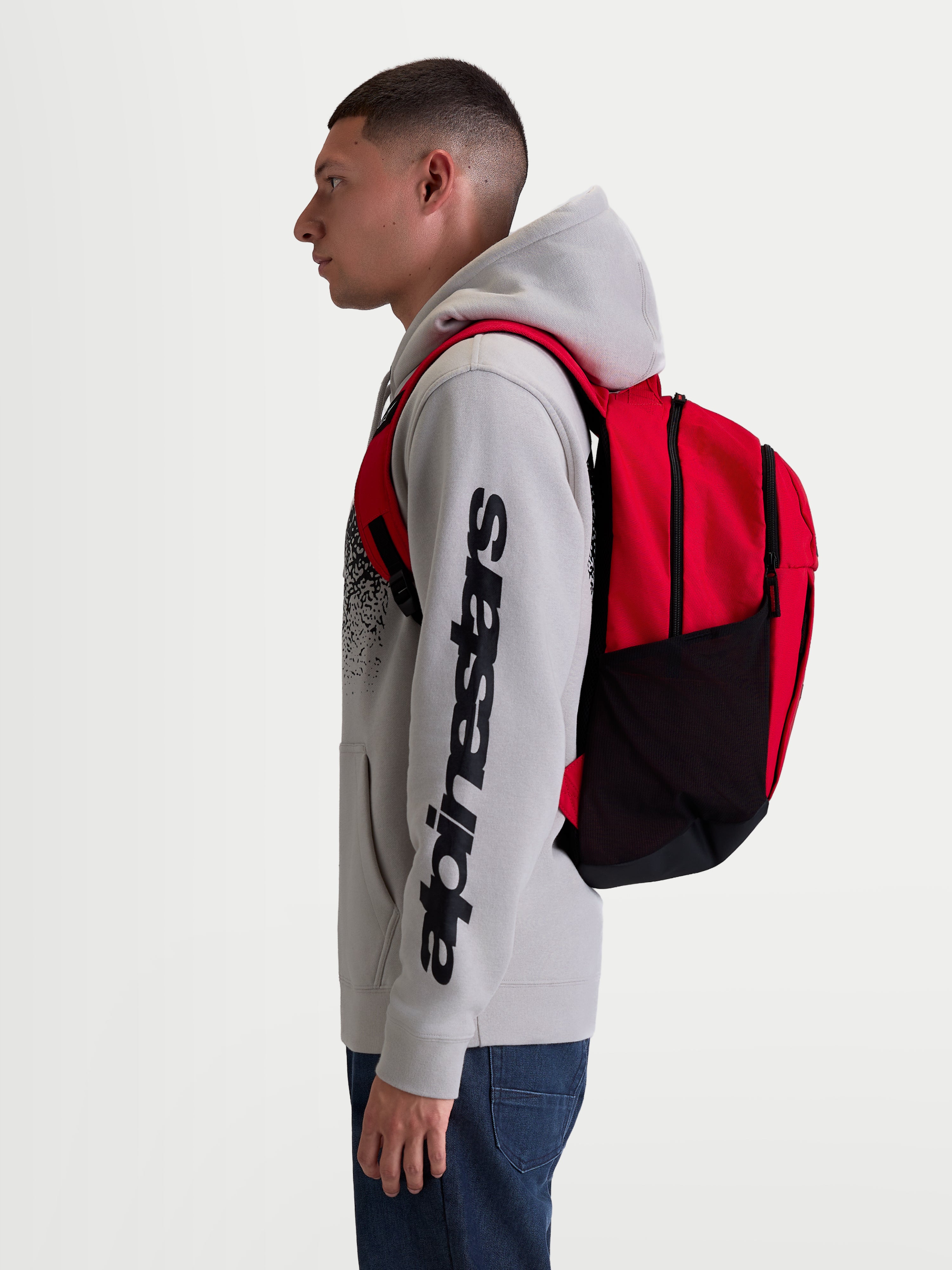 Alpinestars GFX Boss rugzak, rode en zwarte sportswear dagrugzak van 20L, duurzaam 600D polyester met zijvakken van mesh en gevoerde luchtmesh schouderbanden, getoond op een model voor dagelijks gebruik.