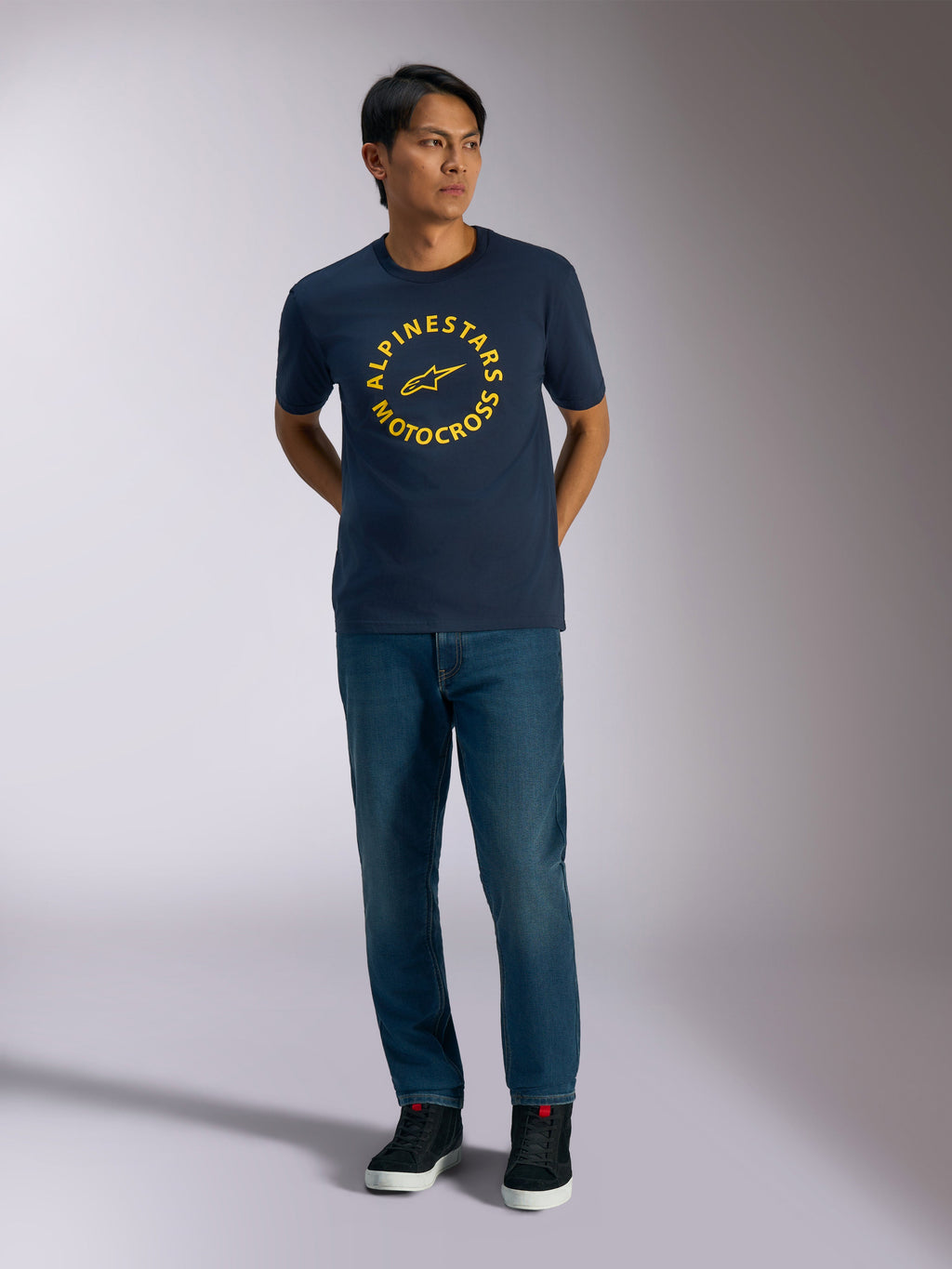 Alpinestars MX CSF Tee, T-shirt met korte mouwen, marineblauw, met een gele cirkelvormige Alpinestars Motocross-graphic, gedragen door een model met blauwe jeans en zwarte sneakers, casual motorsport streetwear