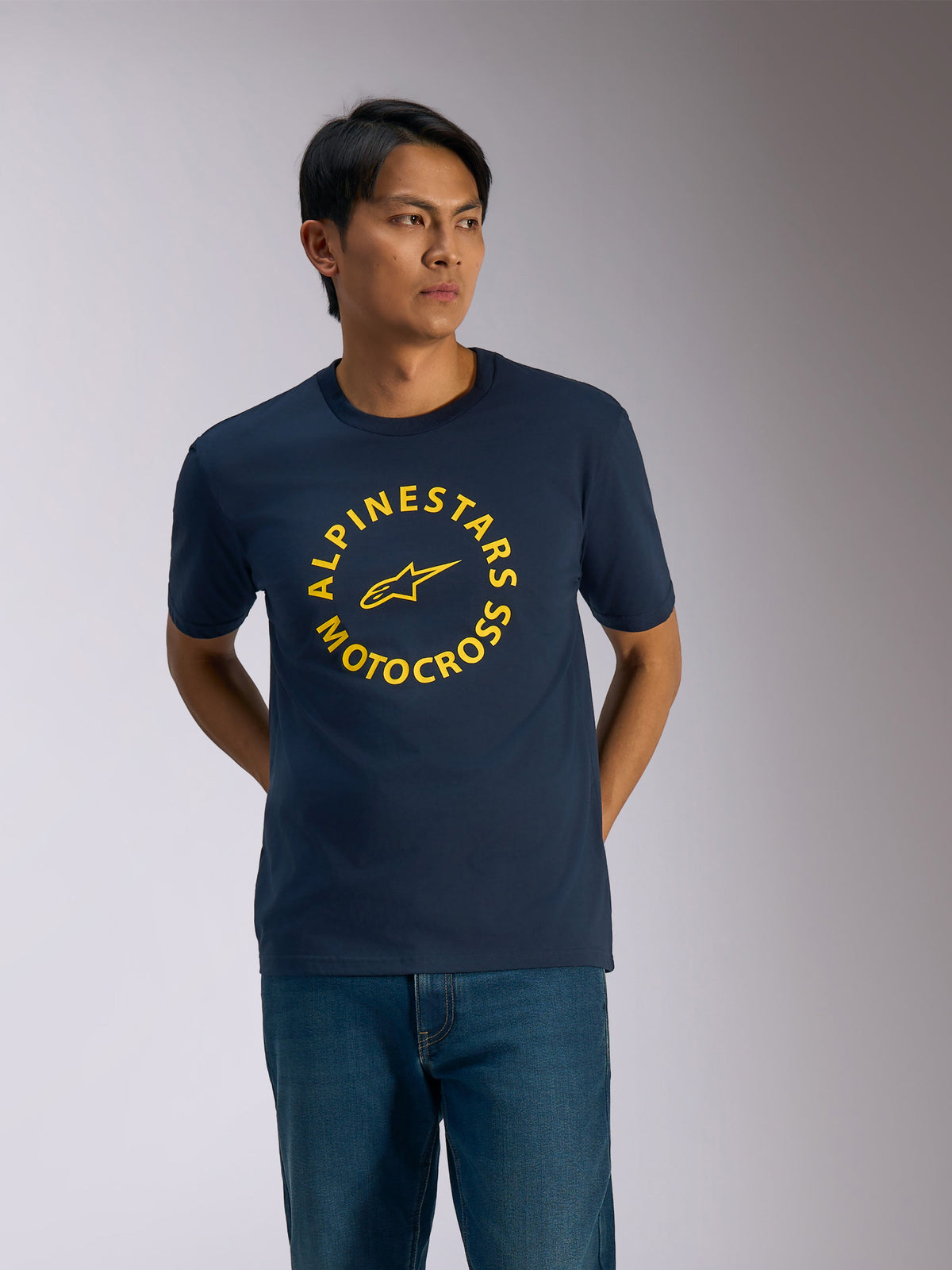 Alpinestars MX CSF Tee, kurzärmeliges T-Shirt, Marineblau, gelbe kreisförmige Alpinestars Motocross-Grafik mit zentralem Stern-Logo, getragen von einem Mann mit blauen Jeans, lässige Motorsport-Streetwear