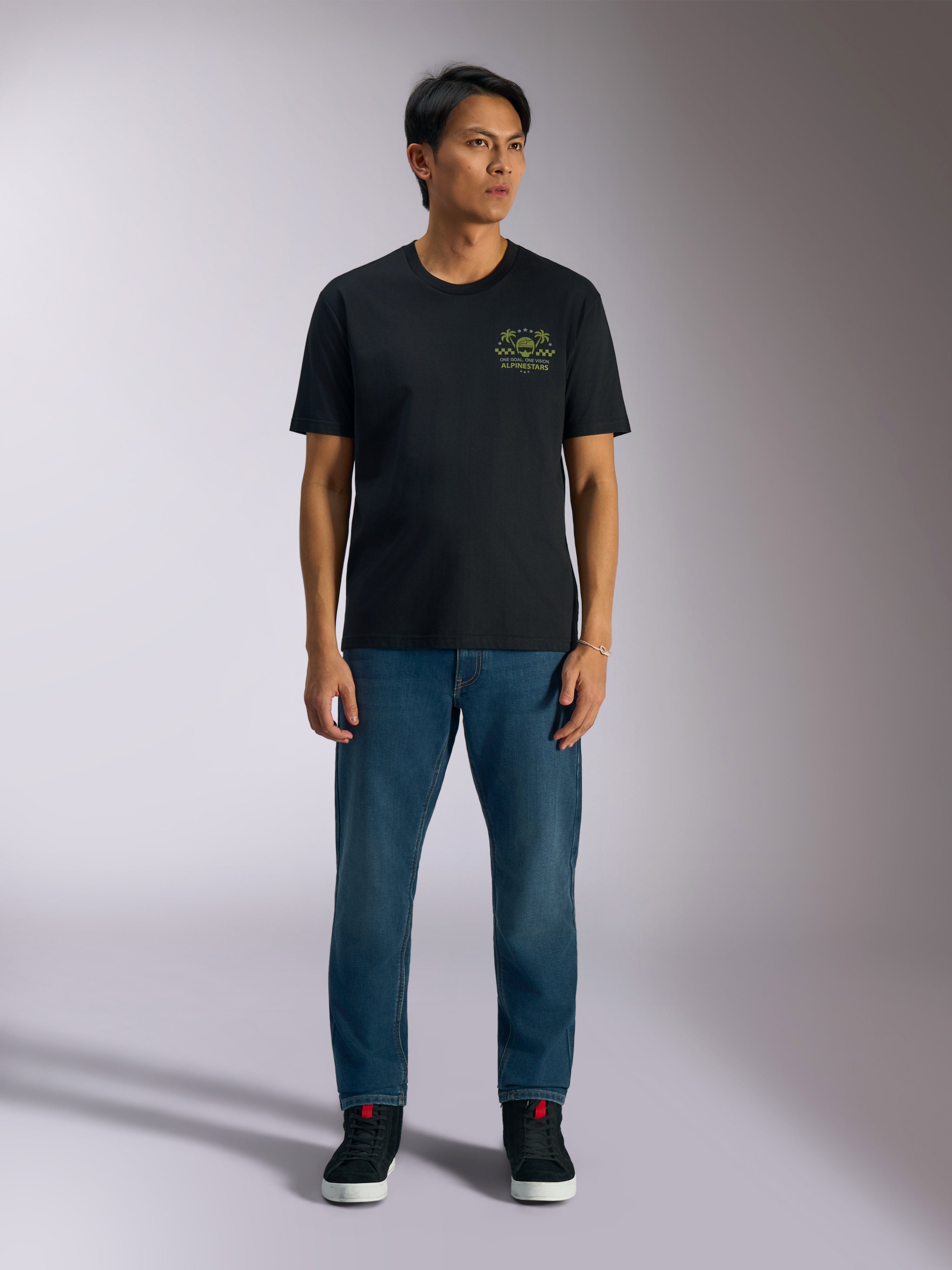 T-shirt Alpinestars Order CSF, t-shirt à manches courtes, noir, motif graphique vert citron avec casque et palmiers sur la poitrine, porté avec un jean bleu et des baskets noires, streetwear motorsport décontracté
