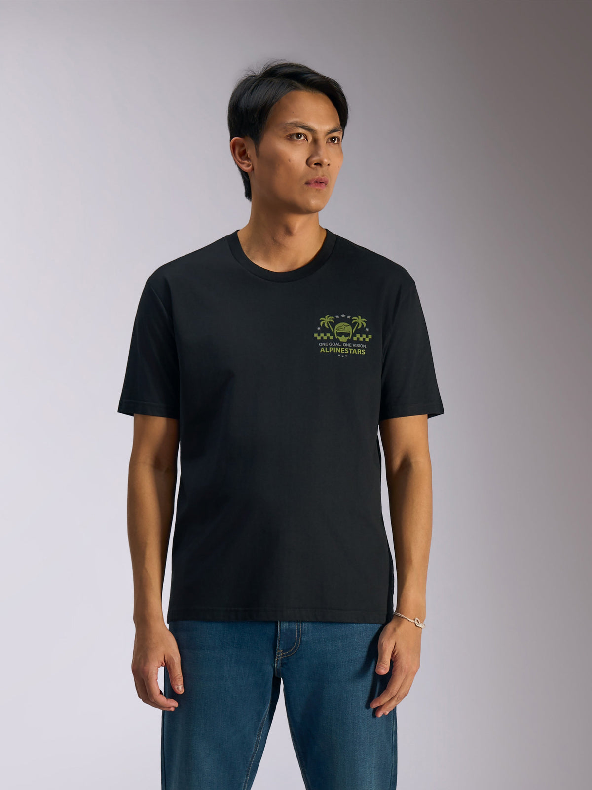 Alpinestars Order CSF Tee, T-shirt met korte mouwen, zwart, groene graphic met helm en palmbomen op de borst, gedragen met blauwe jeans, casual motorsport streetwear