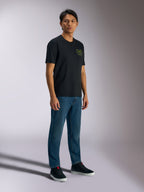 Alpinestars Order CSF Tee, t-shirt à manches courtes, noir, avec logos verts représentant un casque et des palmiers sur la poitrine, style streetwear décontracté, porté avec un jean bleu et des baskets noires