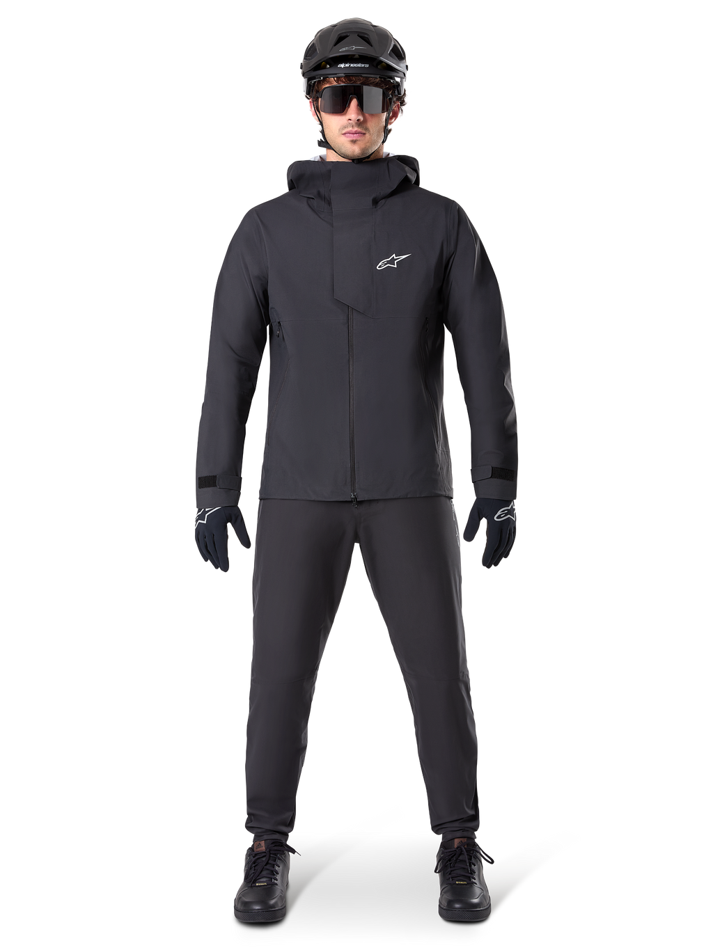 Veste imperméable Alpinestars A-Dura Elite, noire, portée avec un pantalon et des gants de cyclisme assortis, casque noir et lunettes de soleil, logo Astars blanc sur la poitrine, design technique haute performance pour le VTT