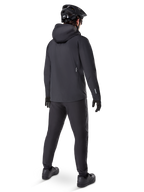 Veste imperméable Alpinestars A-Dura Elite, noire, vue de dos montrant la capuche par-dessus le casque et l'ourlet arrière plus long, associée à un pantalon de VTT, des gants et un casque noirs assortis pour une protection complète sur les sentiers par tous les temps.