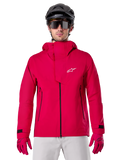 Alpinestars A-Dura Elite Waterproof Jacket, veste de pluie pour VTT, rouge fluo, col montant avec logo Alpinestars blanc, fermetures éclair noires, portée avec gants assortis et casque de vélo noir, équipement de cyclisme technique imperméable