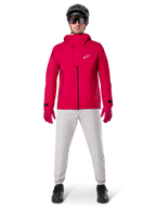 Veste imperméable Alpinestars A-Dura Elite, rouge fluo, veste technique de VTT portée avec un casque de VTT noir, des lunettes de soleil, des gants rouges assortis et un pantalon gris clair, vue d'ensemble de l'équipement de cyclisme toutes saisons